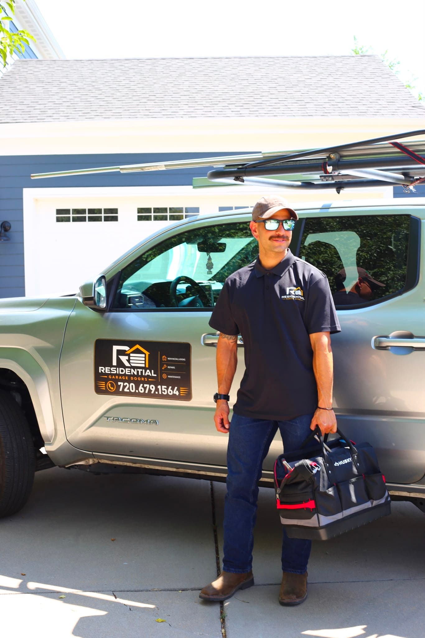 Residential Garage Doors technician in branded uniform standing next to a company truck with tool bag in hand